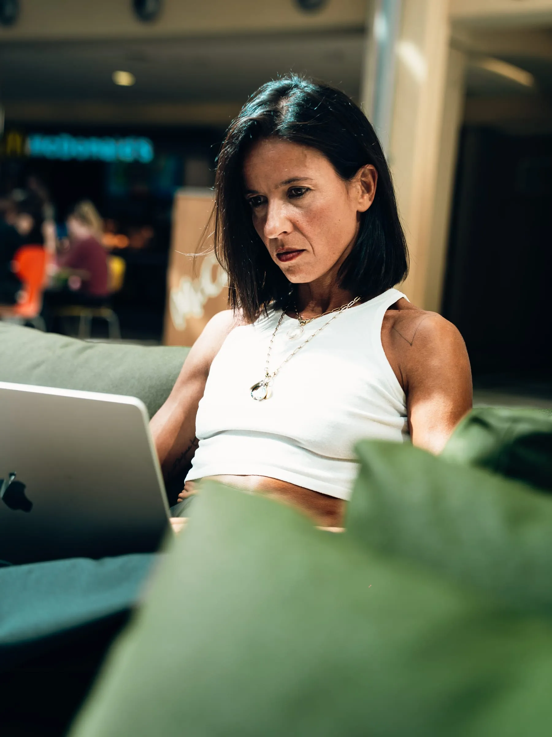 Sara Anna Bocchino al computer, concentrata, seduta su un divano verde in una galleria piena di luce.